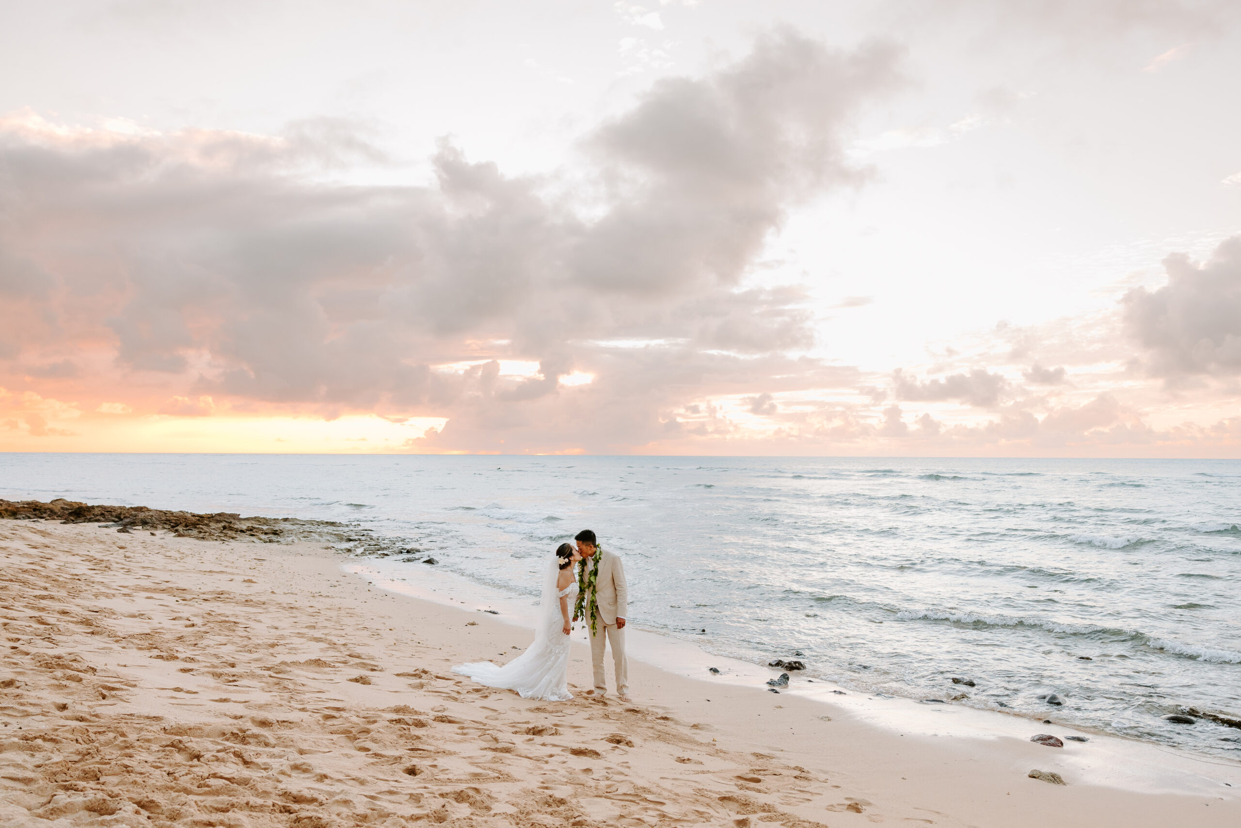 A newly married couple kissing on the beach at sunset on Oahu.